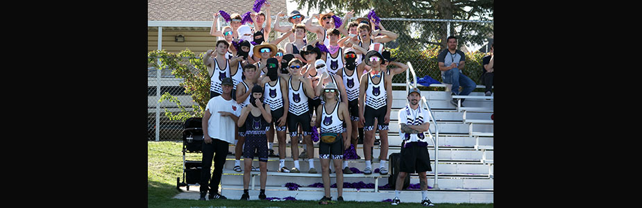 The boys wrestling team in their uniforms on the stands at a girl's soccer game.